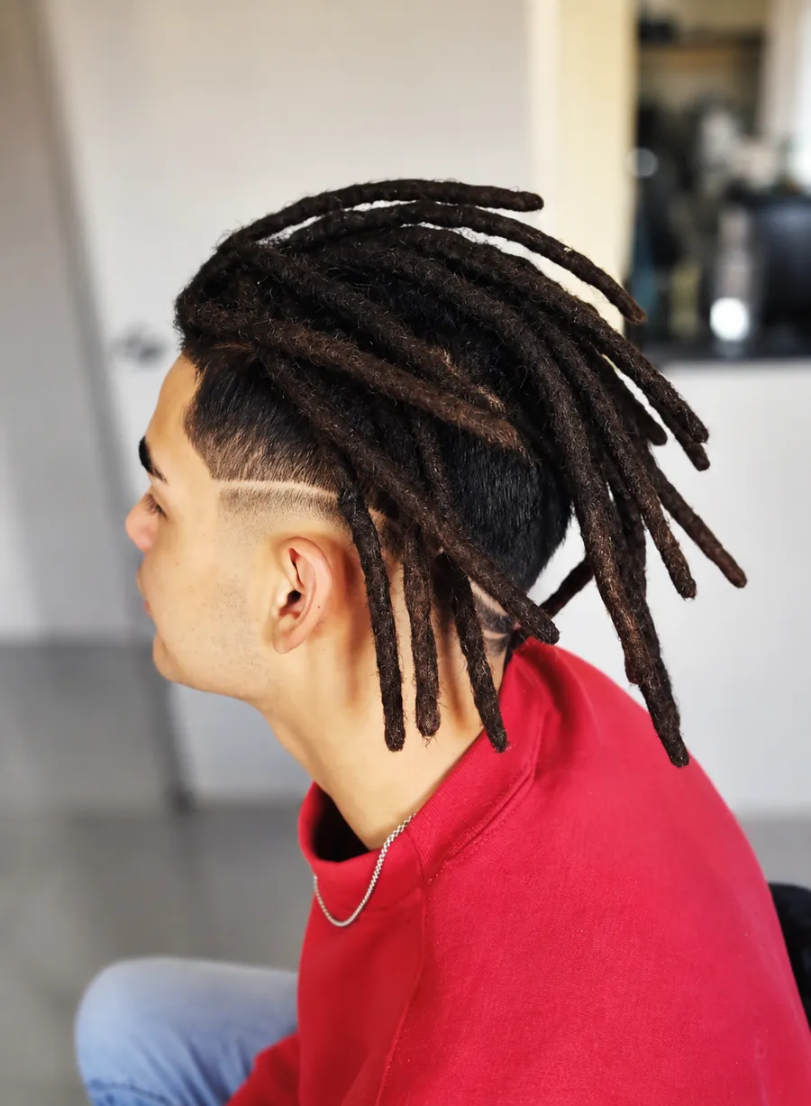 Joven de perfil con dreads castaños largos sobre un degradado